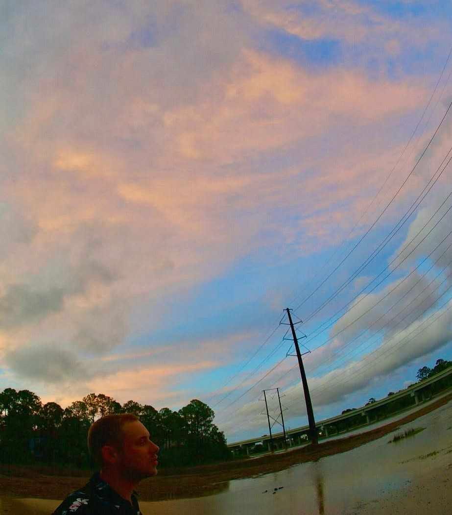 Nick Poulin under a pink and blue dusk sky, marsh water and power lines behind him